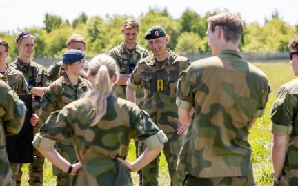 En gruppe personer i milit&aelig;r uniform som st&aring;r ute p&aring; gresset. 