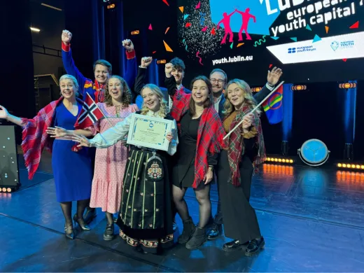 7 pent kledde mennesker st&aring;r p&aring; en scene og jubler over &aring; ha vunnet tittelen europeisk ungdomshovedstad 2026.