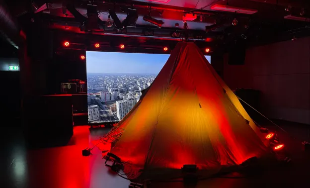 Bildet viser hvordan Coffee in Gaza-installasjonen ser ut. Lavvo i midten med en storskjerm bak som viser Gaza, det er lyssatt med varme lys.